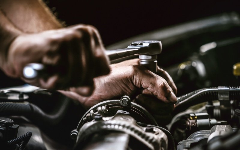 A close-up of a mechanic's hands using a socket wrench to tighten something inside a car's engine compartment.