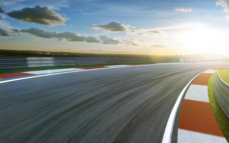 A point of view of a race track circuit corner with red and white line barriers and metal guardrails.