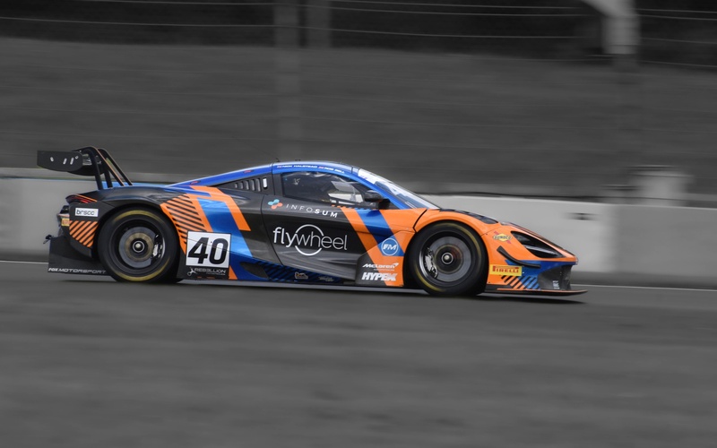 A side view of a black, orange, and blue sports race car with a large rear-wing spoiler on a race track.