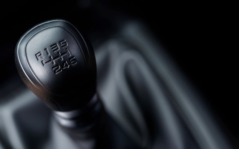 A close-up of a black leather automotive gear shifter stick with the six gears and reverse engraved into the leather.