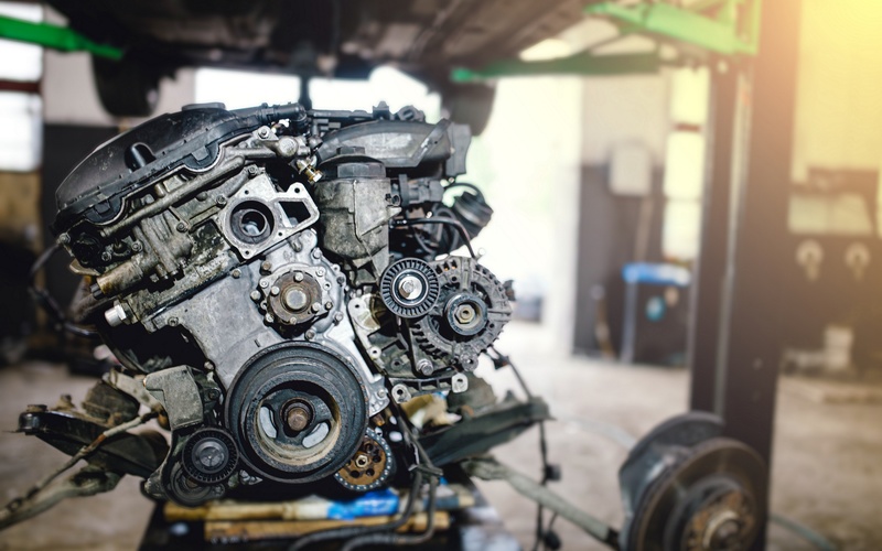 An automotive engine block rests on a pulley underneath a lifted vehicle for installation in an auto repair workshop.