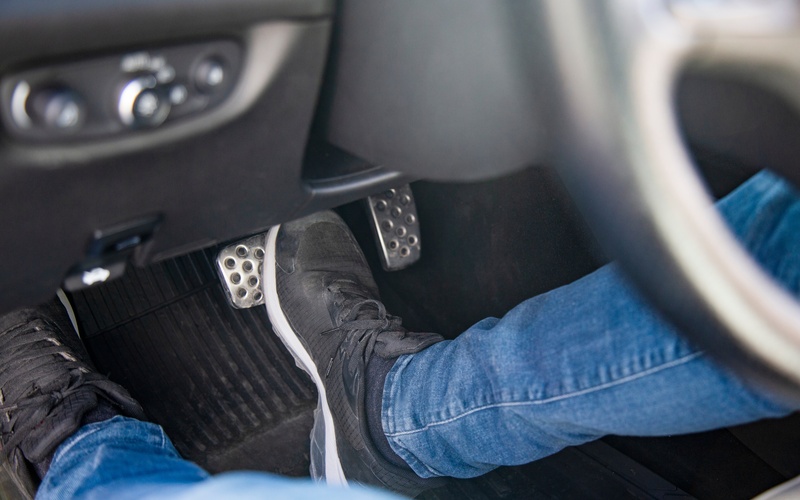 A close-up of a man's feet in the driver's-side cockpit of a car operating the brake and clutch pedals of a car.