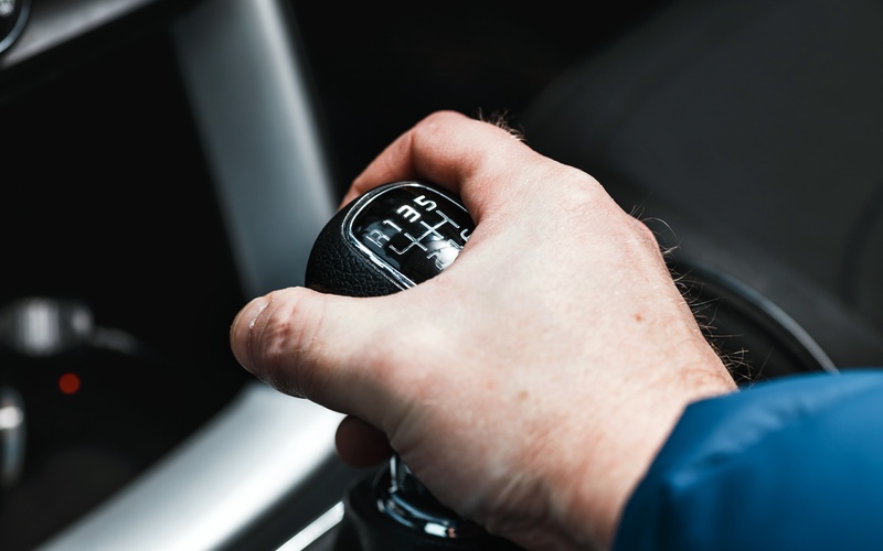 A man's hands firmly grasping the black and silver six-speed stick shift of a modern car with numbers and letters.