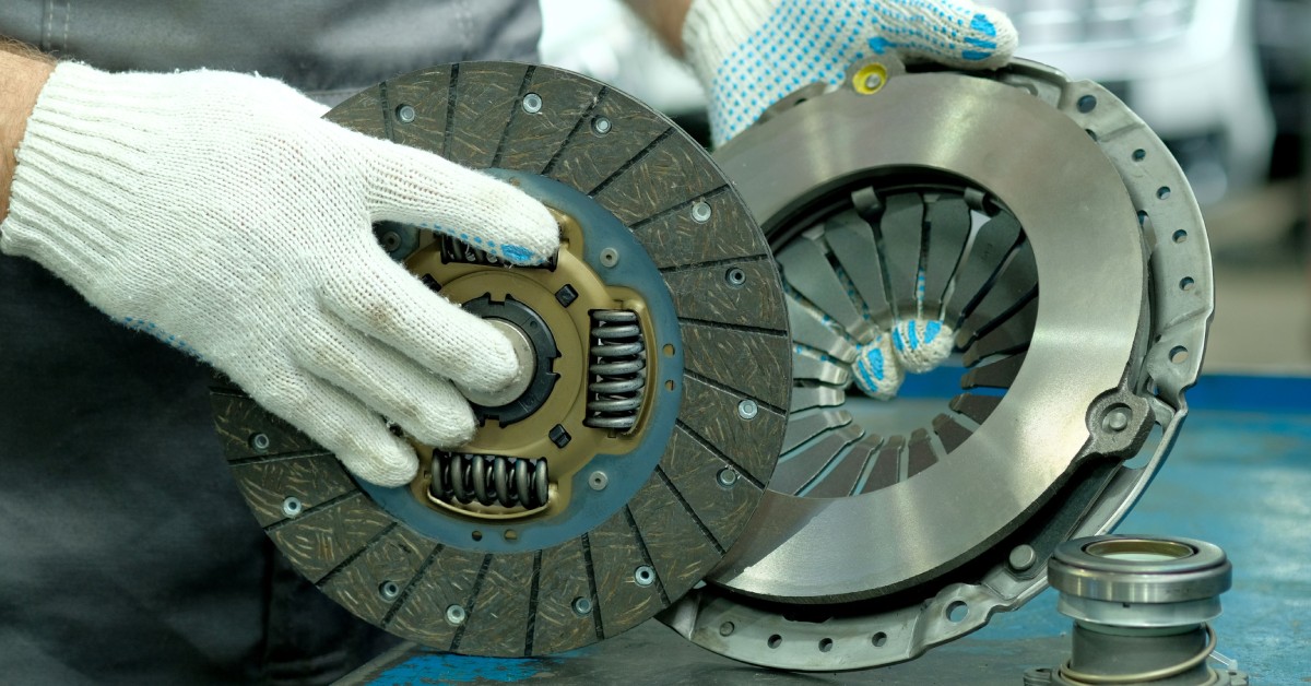 A man with white gloves holding the drive disc and driven disc of a clutch kit with the exhaust bearing on a table.