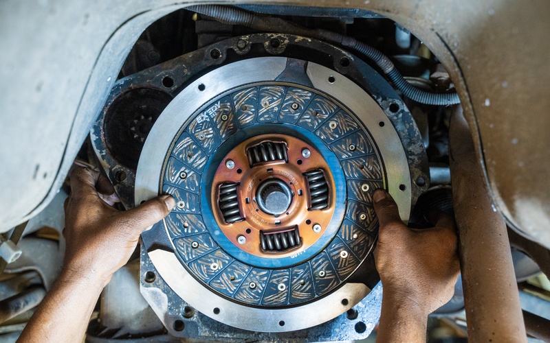 A close-up of a mechanic's hands as they install a new clutch plate and system into a car elevated by a lift.