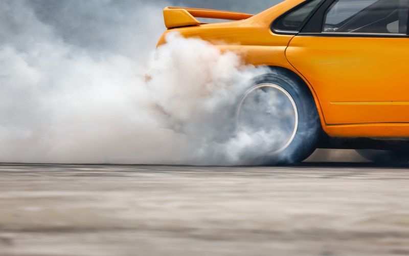 A low, ground-level view of a yellow sports car with a spoiler as its rear tires accelerate and produce lots of smoke.