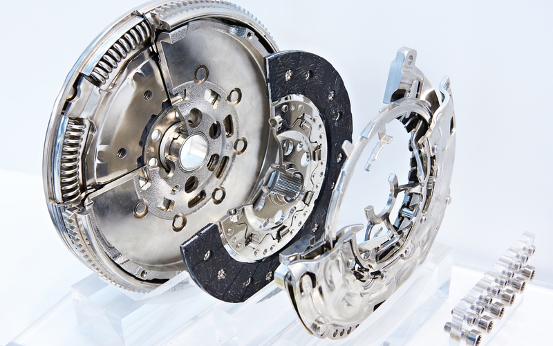 A display of a sectioned automotive clutch system with a dual mass flywheel on plastic stands against a white background.