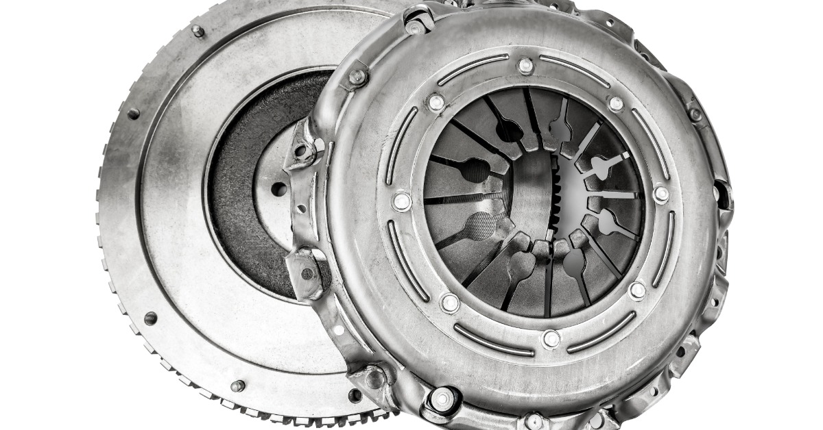 A close-up of a car clutch, including the flywheel and clutch disk, isolated against a blank white background.
