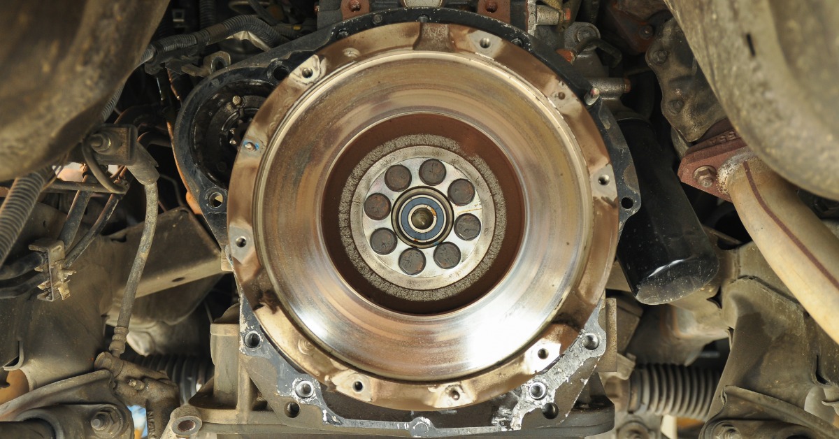A close-up of the undercarriage of an old mini-truck with a focus on the manual clutch and flywheel.