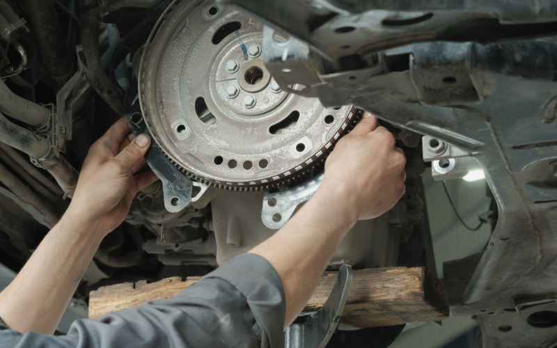 A close-up of a pair of hands reaching into the transmission plate underneath a car elevated on a lift.