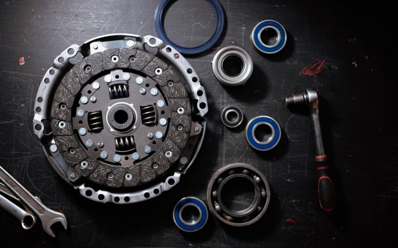 An overhead view of a new clutch kit on a black table, featuring the flywheel bearing and various wrenches.
