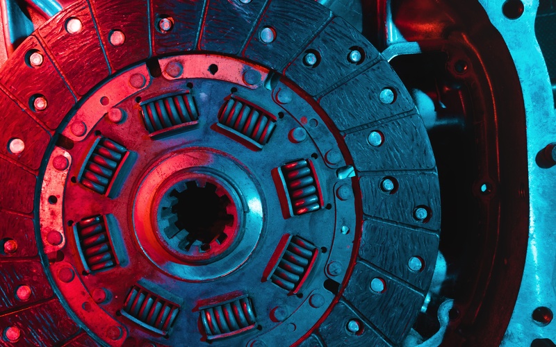 A close-up of an automotive clutch disc disconnected from a car bathed in red and blue light from an external source.