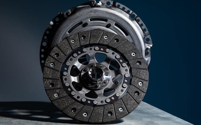 An automotive clutch disc and clutch basket disconnected from a car displayed upright against each other.