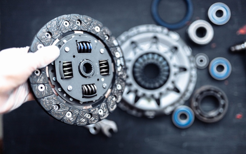 A close-up of a hand with a white latex glove holding a car clutch disc over other clutch components for a kit.