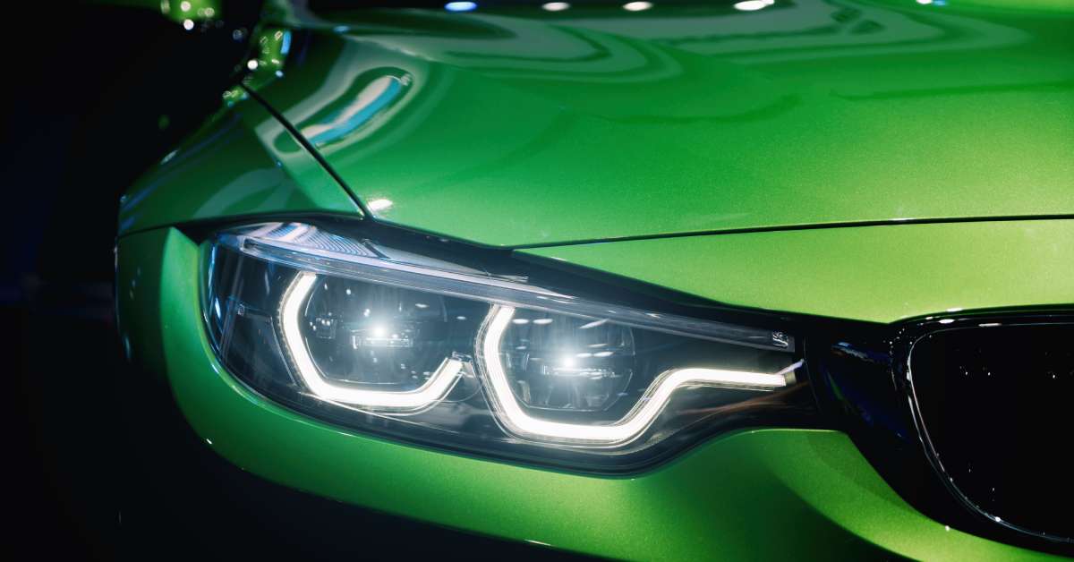 The front headlight profile of a lime green car featuring the BMW headlight design with the headlights activated.