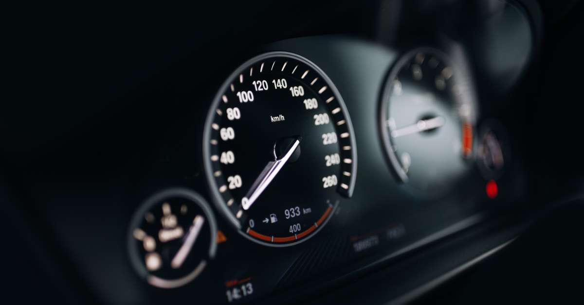 The driver's dashboard of a sports car featuring the speedometer, tachometer, and gas tank gauge with the gauges illuminated.