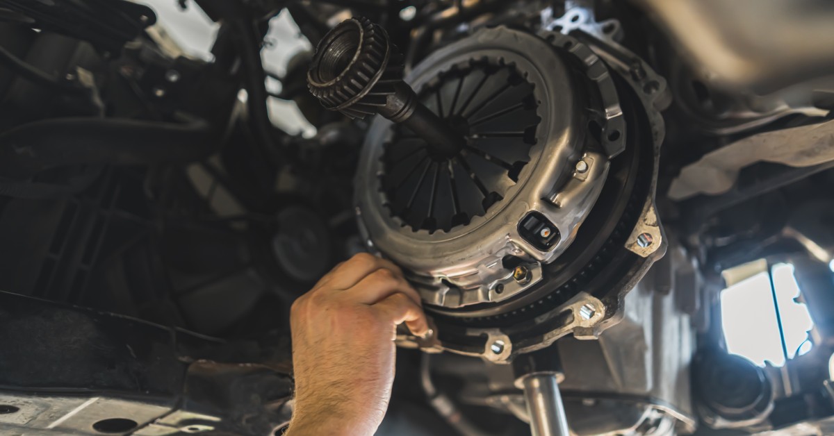 A mechanic is installing a new performance clutch underneath a vehicle suspended on a lift in a repair shop.