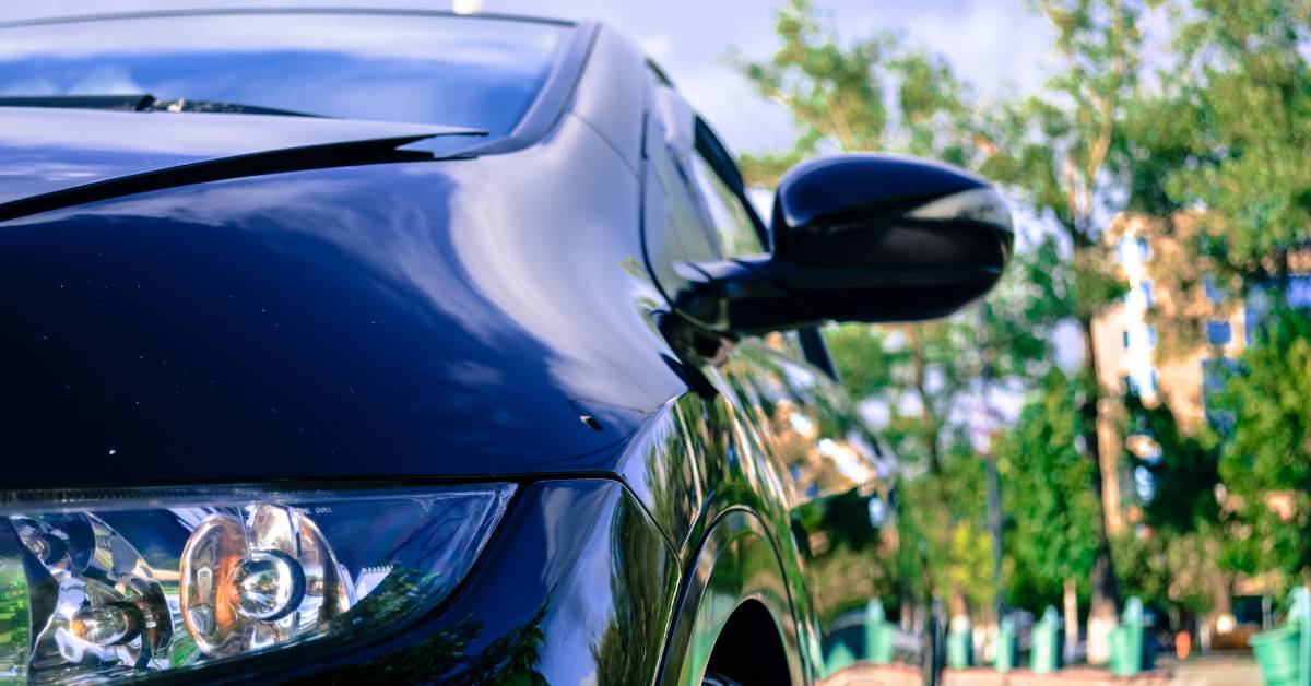 A quarter of the front end of a dark blue Honda civic with a brick path and trees blurred behind it.