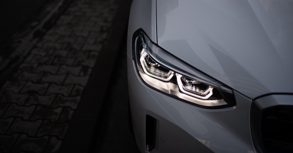 An overhead quarter profile view of a white BMW at night emphasizes the headlight, which is activated.