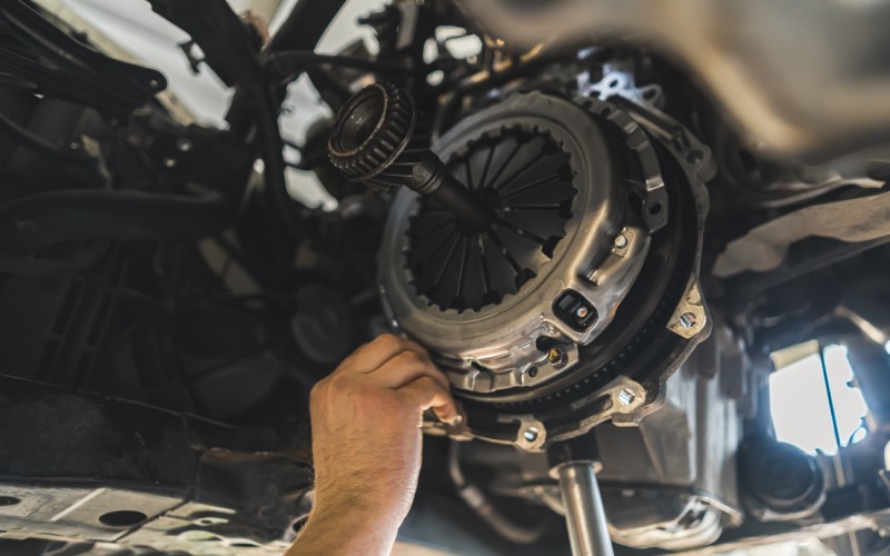 A hand is grabbing a high-performance automotive clutch underneath a lifted car during clutch installation.