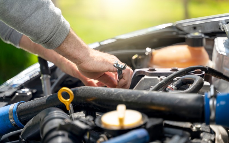 A man's forearms, his gray sleeves pushed up them as his hands hold a wrench and work on an engine in a vehicle.