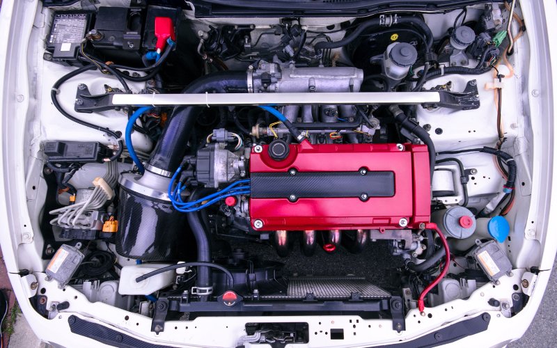 An overview of the open engine compartment of a white Honda Integra B18 car with a red engine cover.