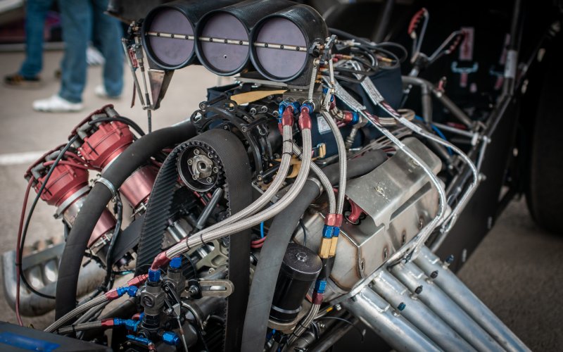 A close-up of a drag racing car's exposed V8 engine. The engine includes air intakes, a supercharger, and more.